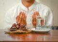 Fast breaking meal or iftar dish with muslim man hands praying to Allah. Dates with a glass of mineral water on the table.Traditional Ramadan, fast breaking meal.Buka puasa or sahur Ramadan concept.