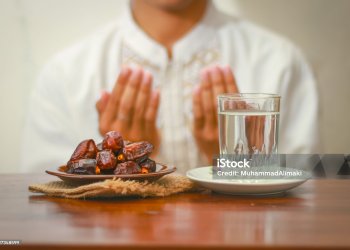 Fast breaking meal or iftar dish with muslim man hands praying to Allah. Dates with a glass of mineral water on the table.Traditional Ramadan, fast breaking meal.Buka puasa or sahur Ramadan concept.