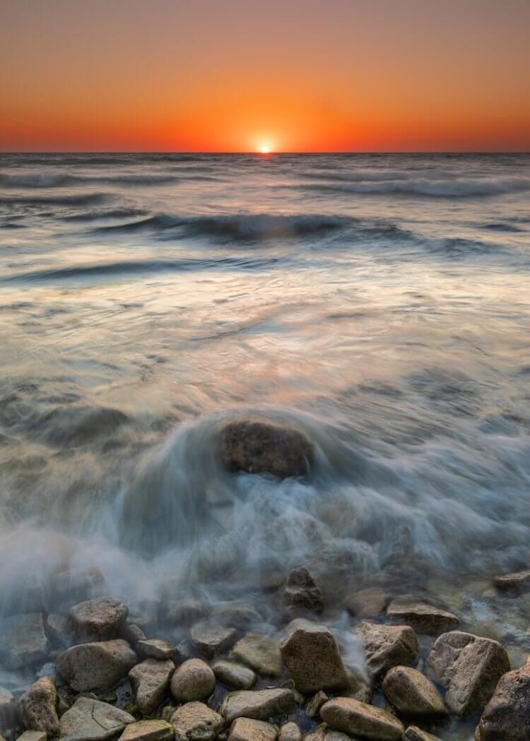 A sunset over the ocean with rocks in the foreground